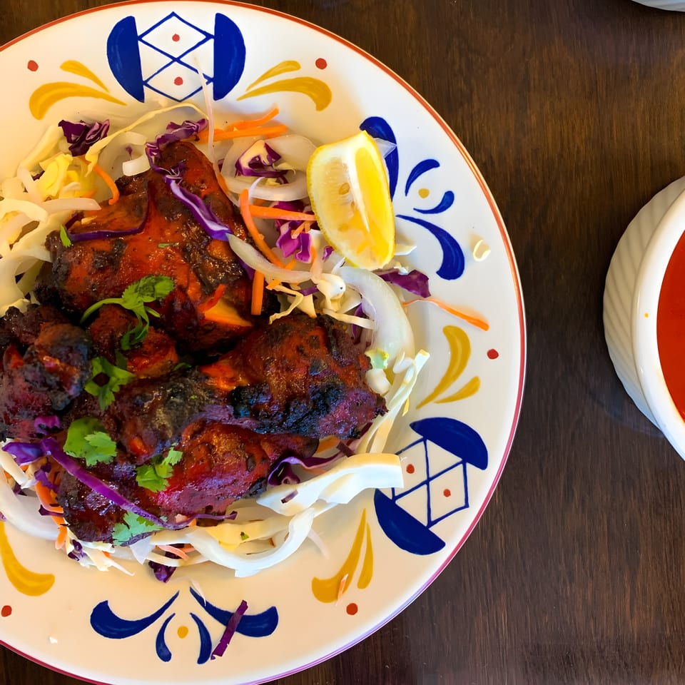 Aroma Indian Cuisine's Tandoori Chicken, garnished with cilantro, lemon, and a side of red sauce.
