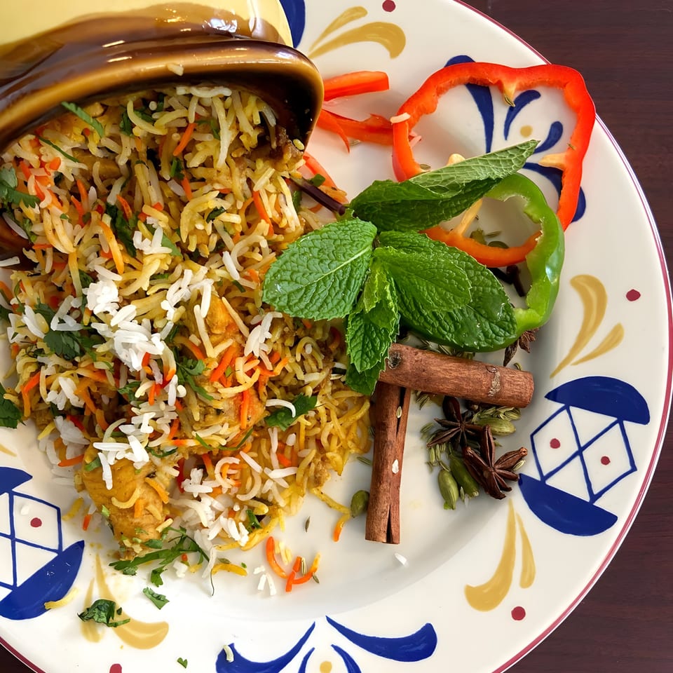 Aroma Indian Cuisine's chicken biryani, garnished with mint, bell peppers, and whole spices on a decorative plate.