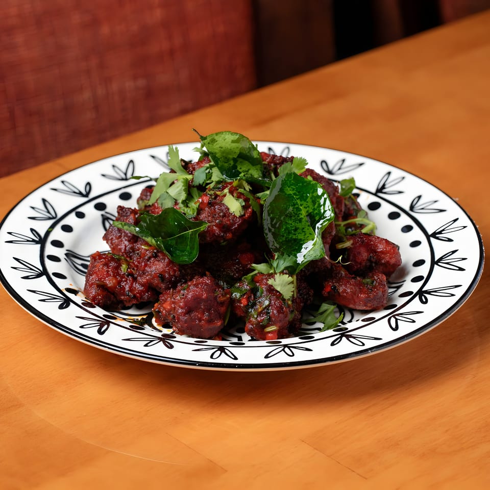 Aroma Indian Cuisine's deep red chicken dish, garnished with fresh green herbs, on a decorative white plate.