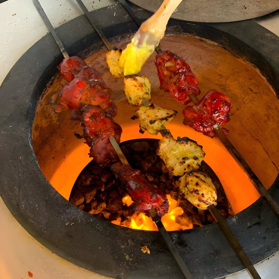 Chicken tikka and tandoori chicken skewers cooking in a fiery tandoor oven at Aroma Indian Cuisine.