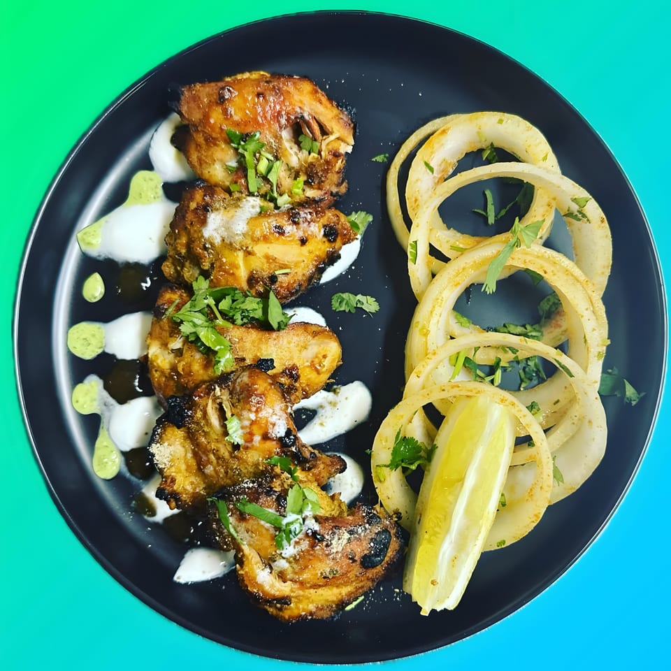 Aroma Indian Cuisine's Tandoori Chicken with onion rings, lemon, and sauces on a black plate.