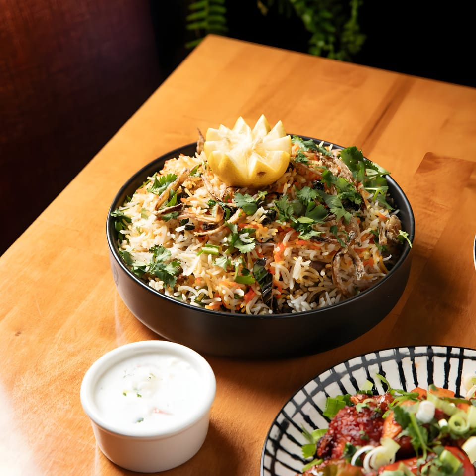 Aroma Indian Cuisine's chicken biryani with a carved lemon, raita, and a side dish.